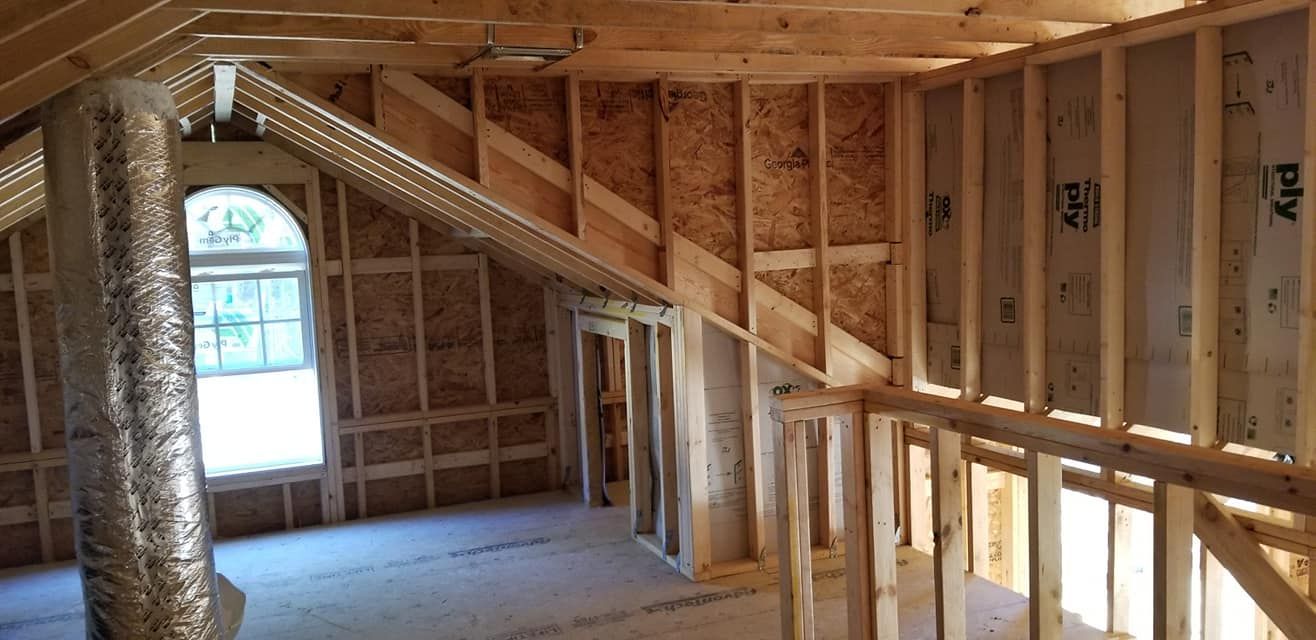 Unfinished attic interior featuring wooden wall framing, sloping rafters, a round-top window, and exposed ductwork.