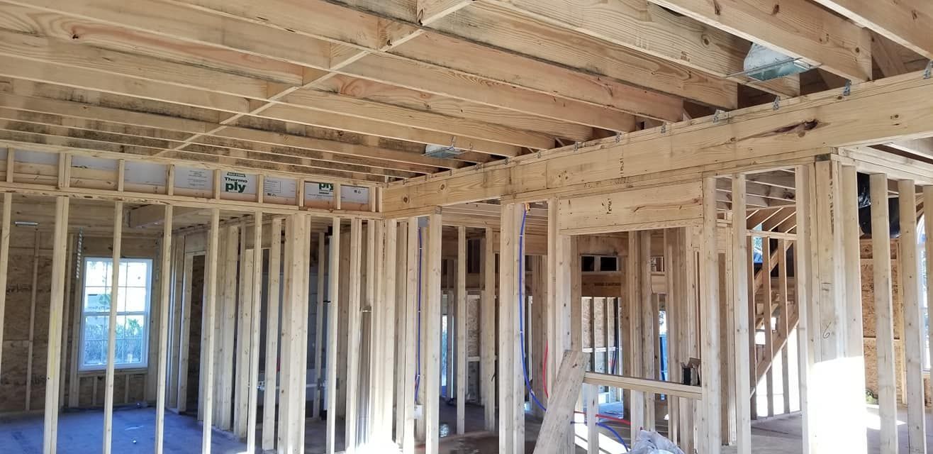 The unfinished interior of a house under construction, featuring exposed wooden wall studs and ceiling joists.