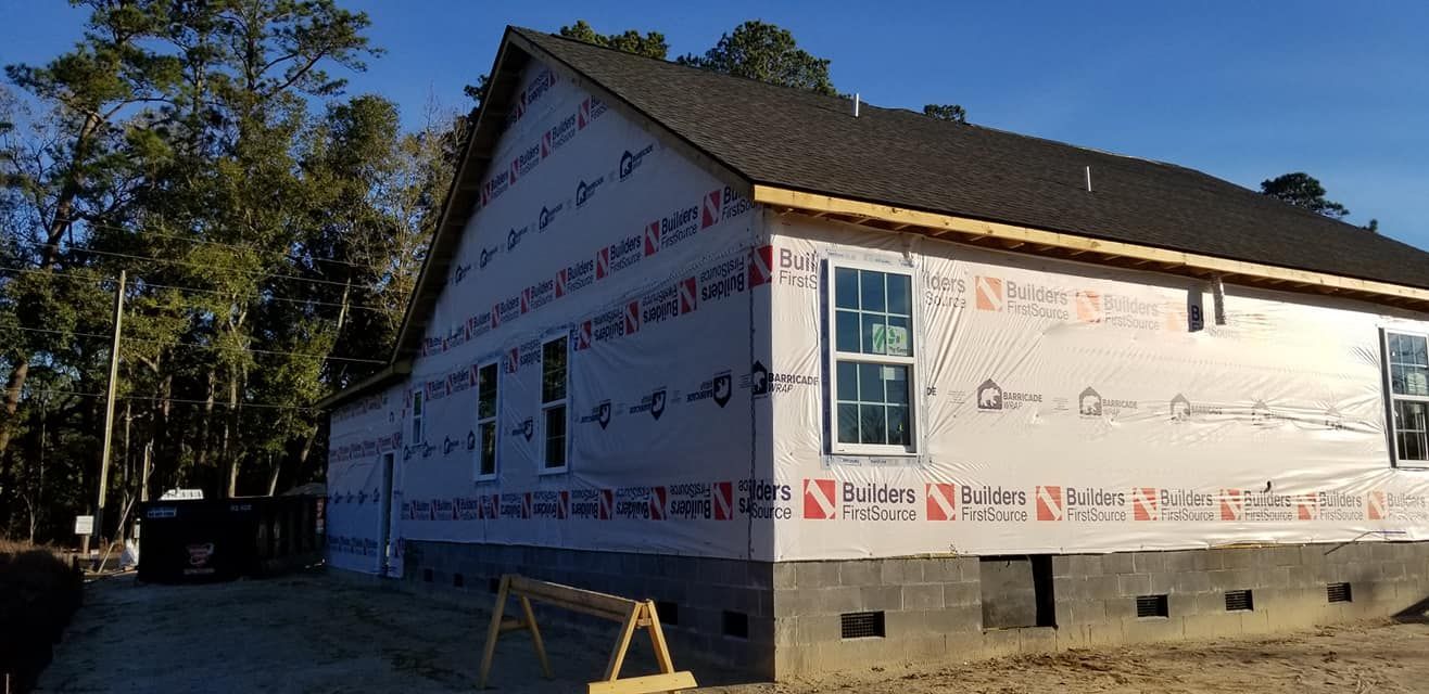 A new residential home under construction, featuring a dark shingled roof, light-colored house wrap, and concrete foundation.