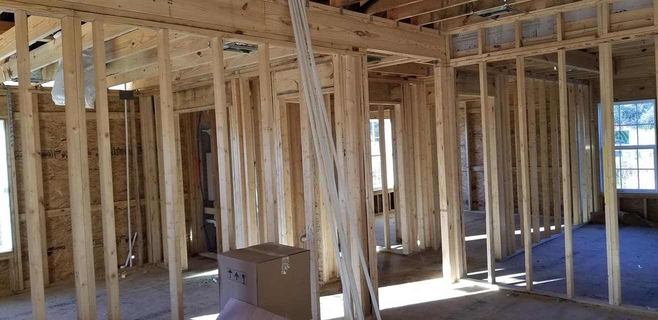 Framed interior of a house under construction with exposed wooden wall studs and ceiling joists.