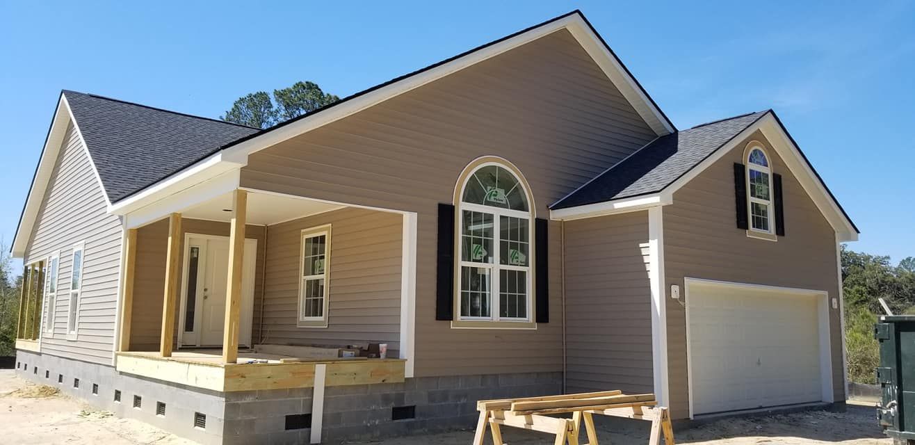 A new single-story house with tan siding, black shutters, a front porch, and an attached two-car garage.