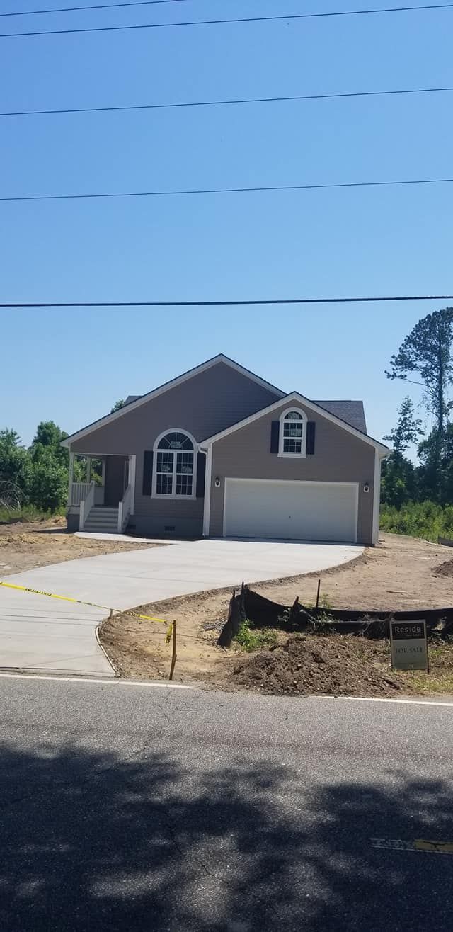 A newly constructed, single-story taupe house with a two-car garage and curved concrete driveway under a clear blue sky.