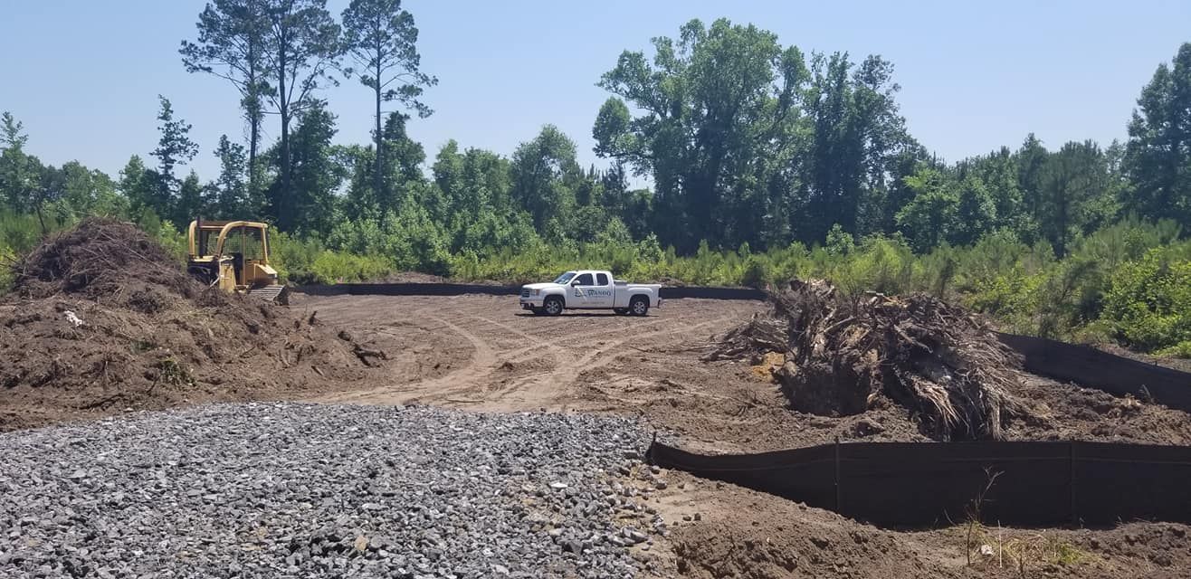 A construction site with a white pickup truck, a yellow bulldozer, mounds of dirt, gravel, and trees in the background.