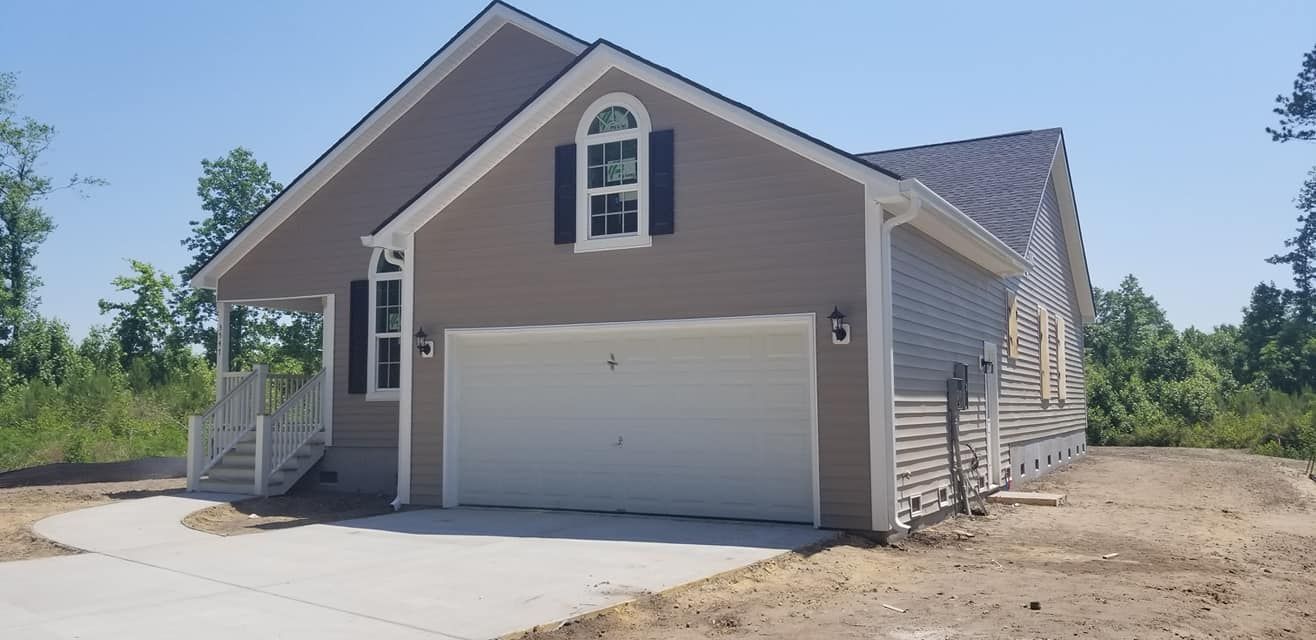 A single-story, beige suburban house with a two-car garage, white trim, and a concrete driveway on a sunny day.