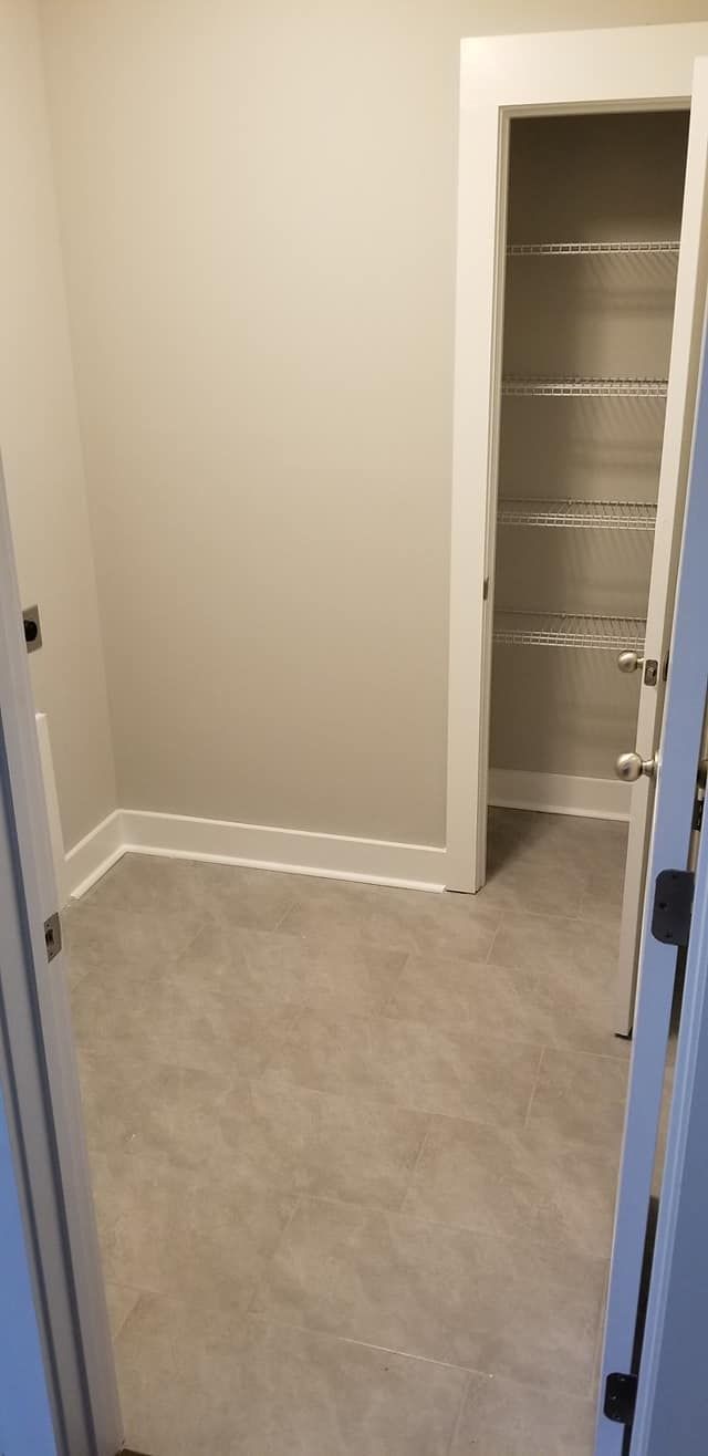 A neutral-toned room with light gray walls, light flooring, and an open doorway leading to a pantry with wire shelving.