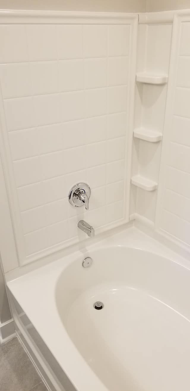 A white bathtub and shower surround with three built-in shelves, a chrome faucet, and a diverter handle.