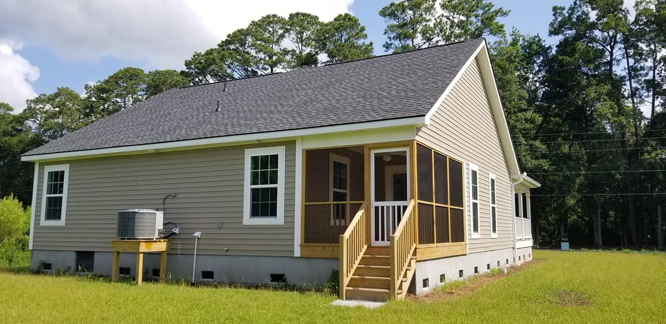 A beige single-story house with a grey roof, a screened-in porch, and an air conditioning unit on a stand in a grassy yard.
