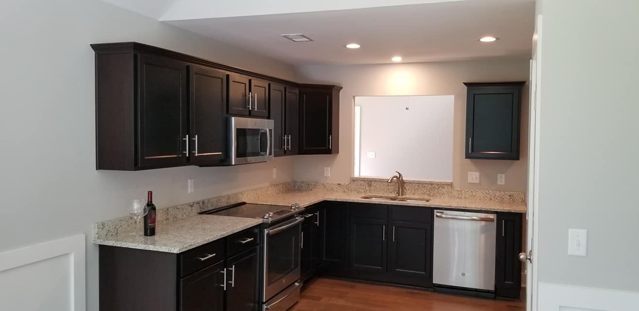 Modern kitchen featuring dark cabinetry, granite countertops, stainless steel appliances, and light gray walls.