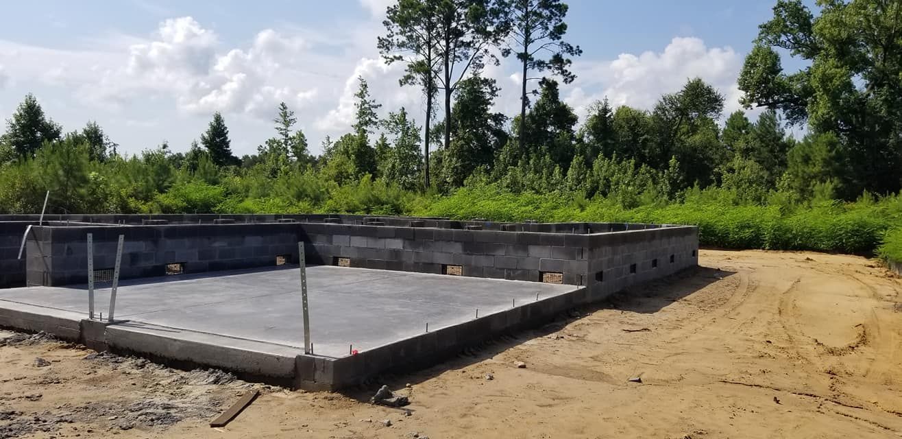 A concrete block foundation for a house under construction in a grassy, wooded lot.