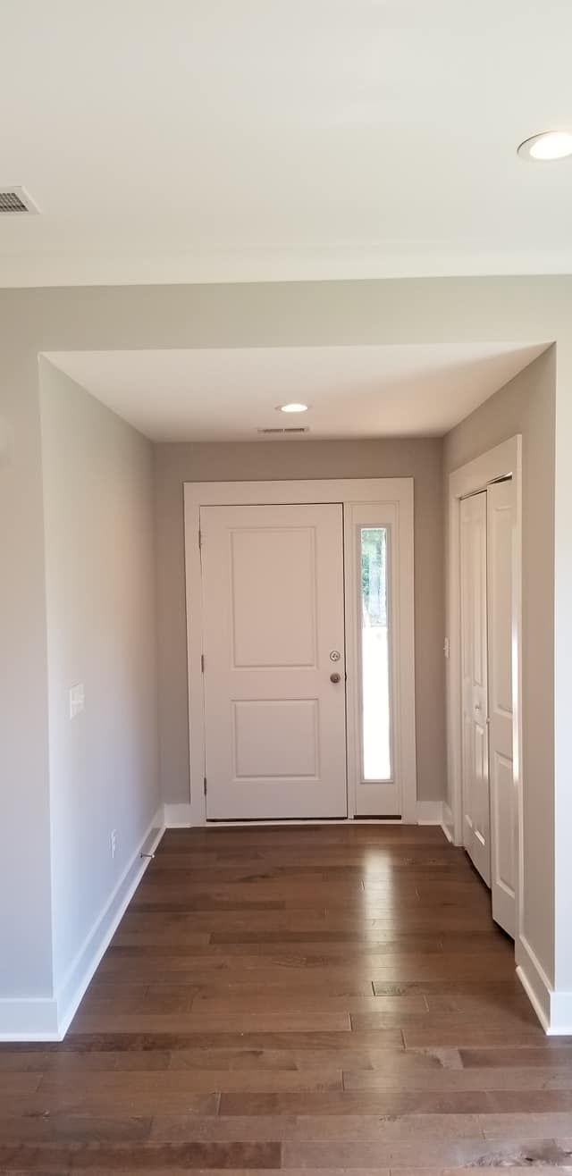 An entryway with hardwood floors, neutral walls, white trim, a front door with a side window, and a closet on the right.