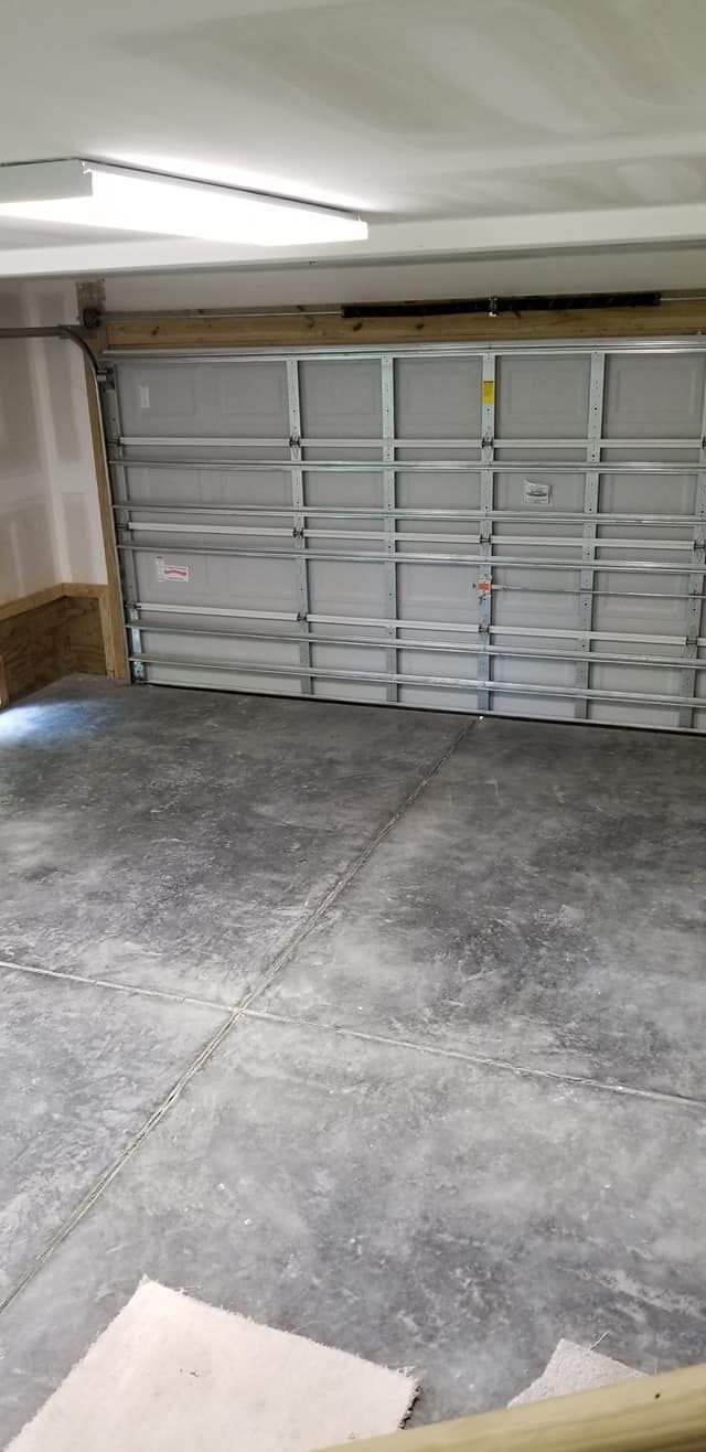 Interior view of a garage with a metal sectional door, gray concrete floor, and overhead light.