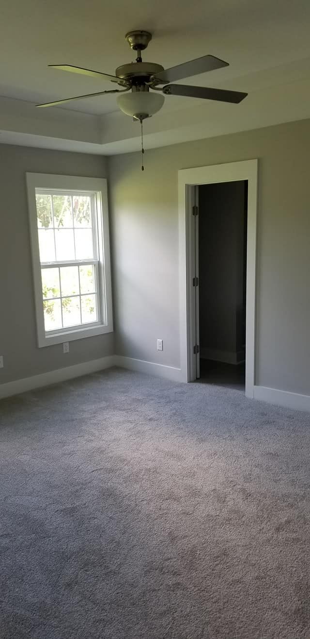 Empty room with light gray walls, gray carpet, a ceiling fan, one window, and an open doorway.