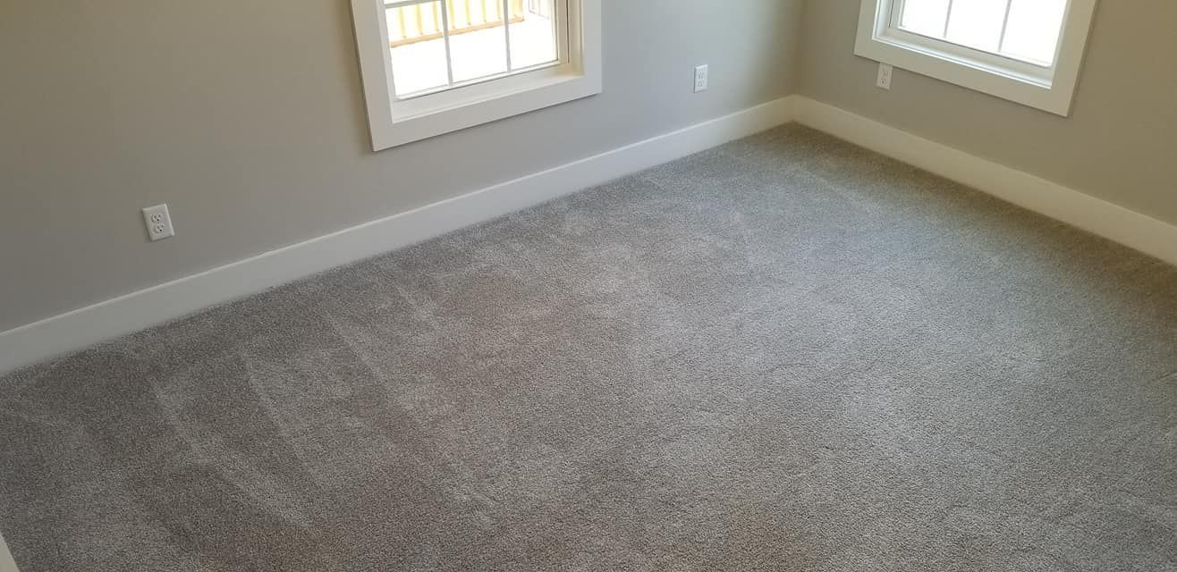 A light-colored, carpeted room with white trim and baseboards and two windows on adjacent walls.