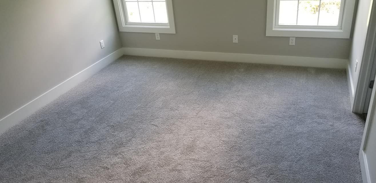 A room with grey walls, white baseboards, two windows, and light grey wall-to-wall carpeting.
