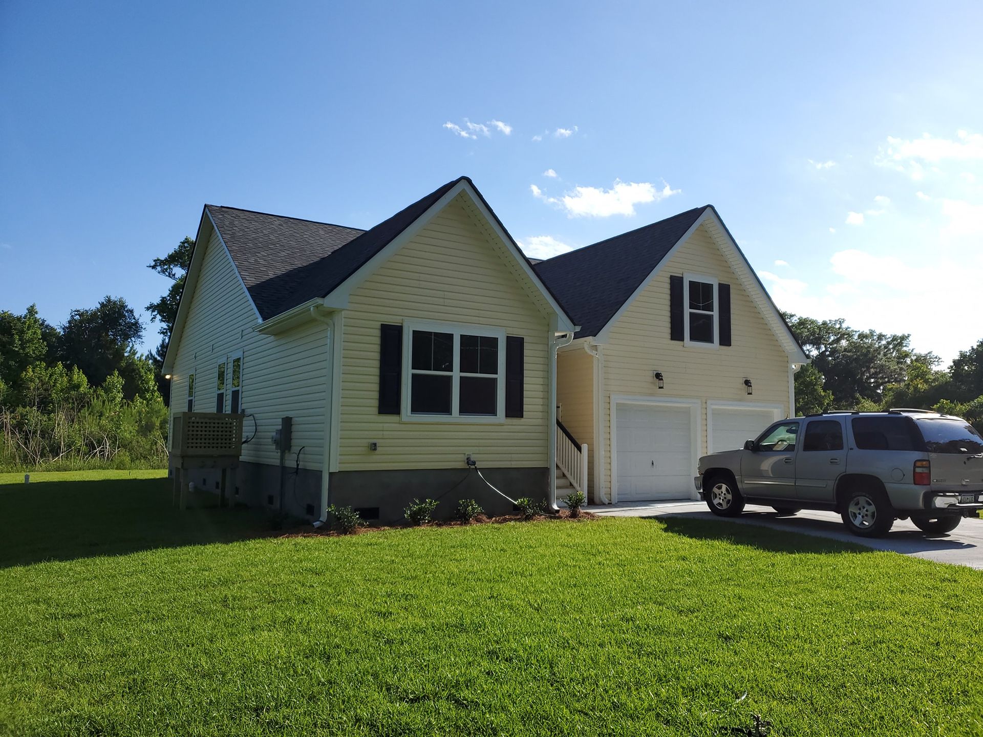 A light yellow house with a gray roof and attached garage, with a silver SUV parked in the driveway on a sunny day.