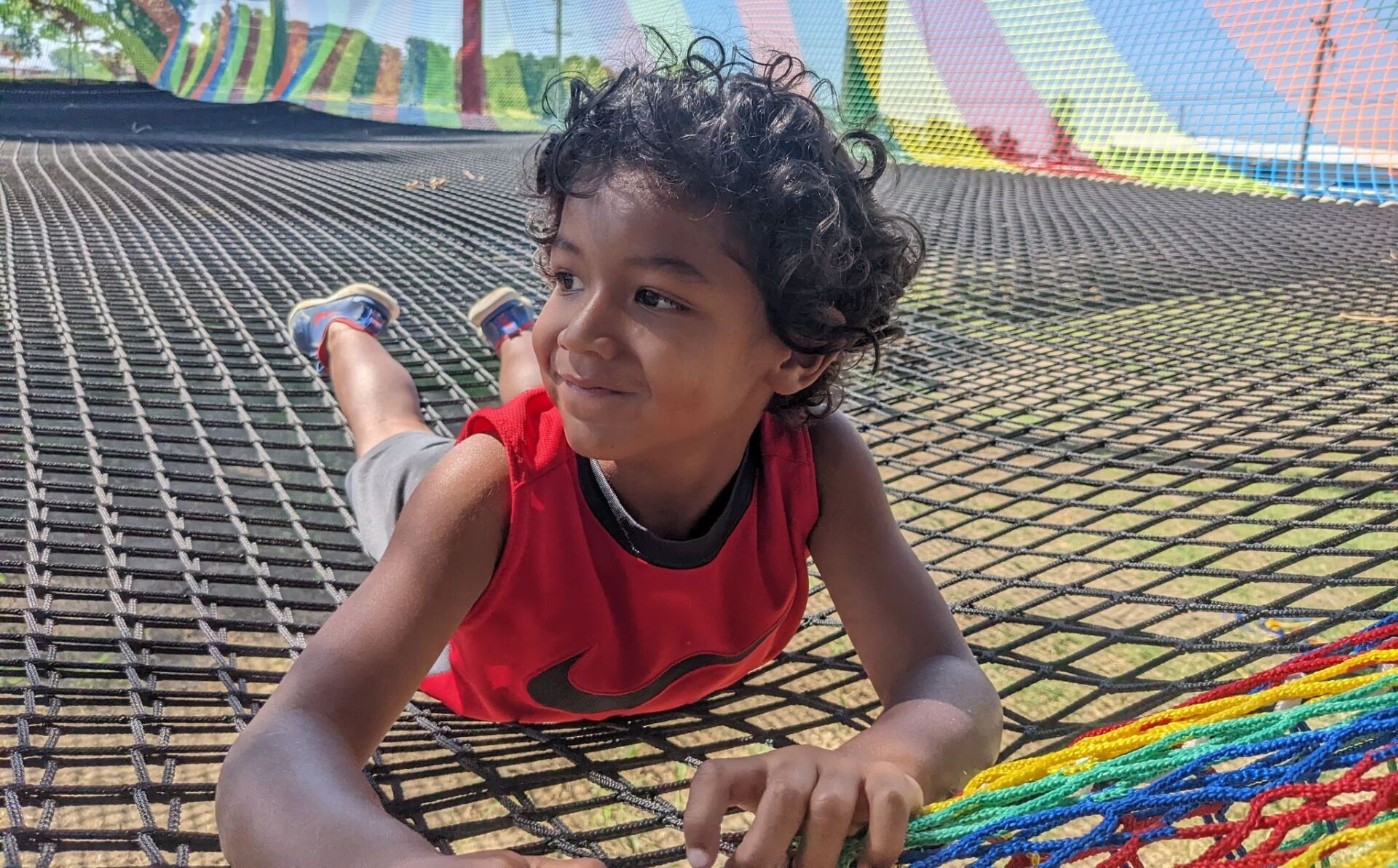 A young boy is laying on a rainbow net.