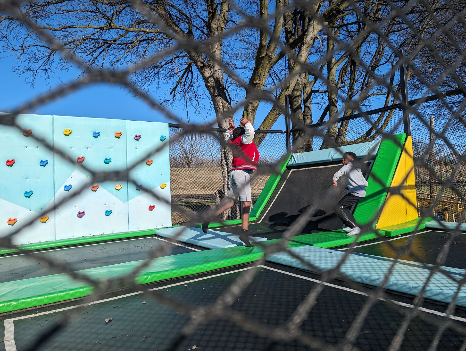 A group of children are playing on a trampoline behind a chain link fence.