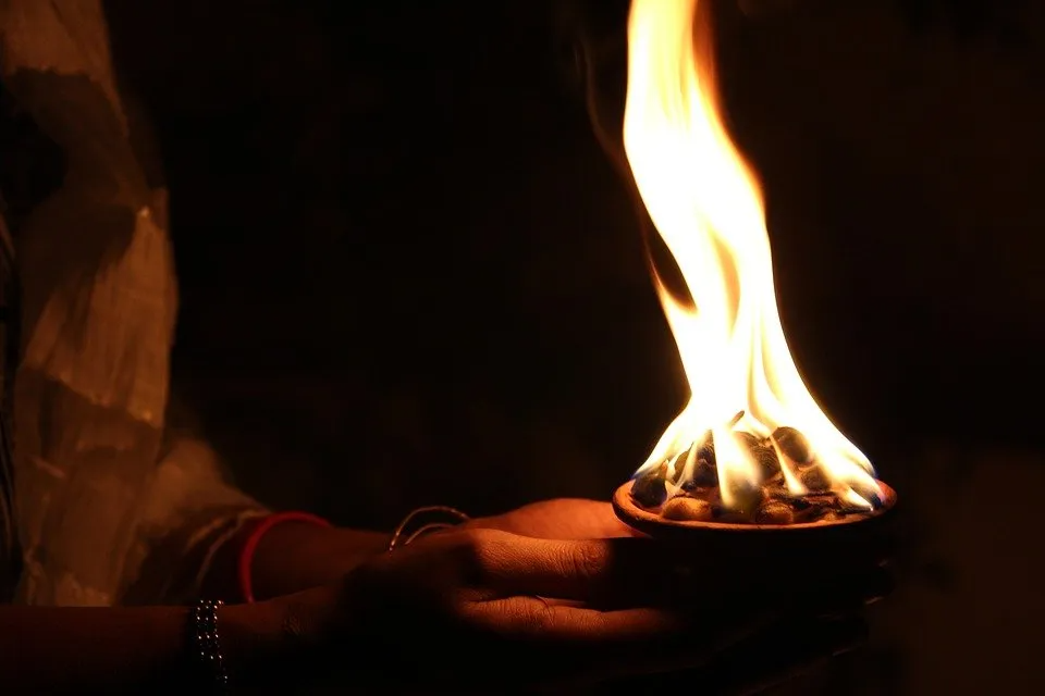 Hand holding a small oil lamp with a bright flame in a dark setting