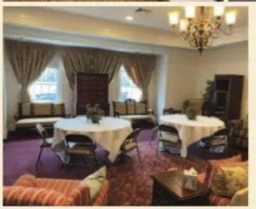 Elegant lounge with round tables, folding chairs, curtained windows, and a chandelier over a patterned carpet.