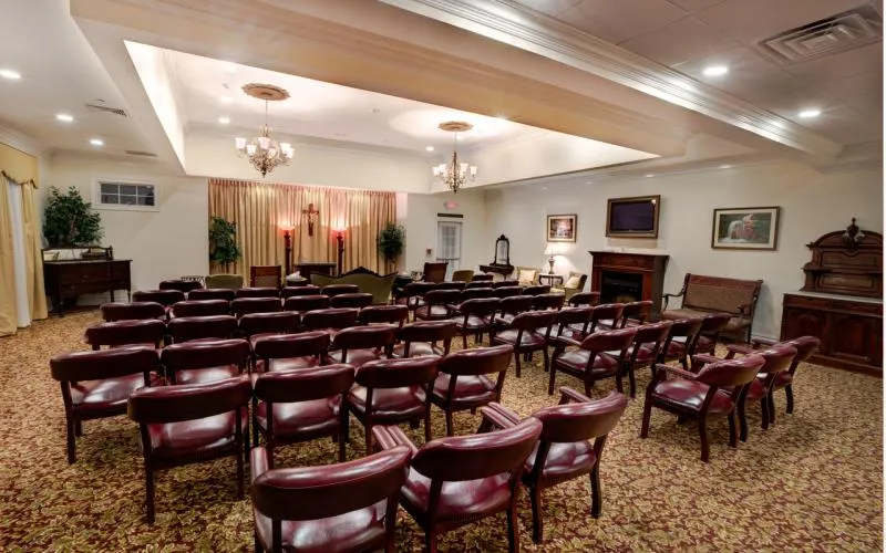 Empty meeting room with rows of brown chairs facing a front wall and fireplace under warm ceiling lights