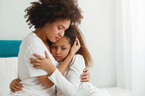 Woman comforting a child in bed, hugging her close in a bright, white room