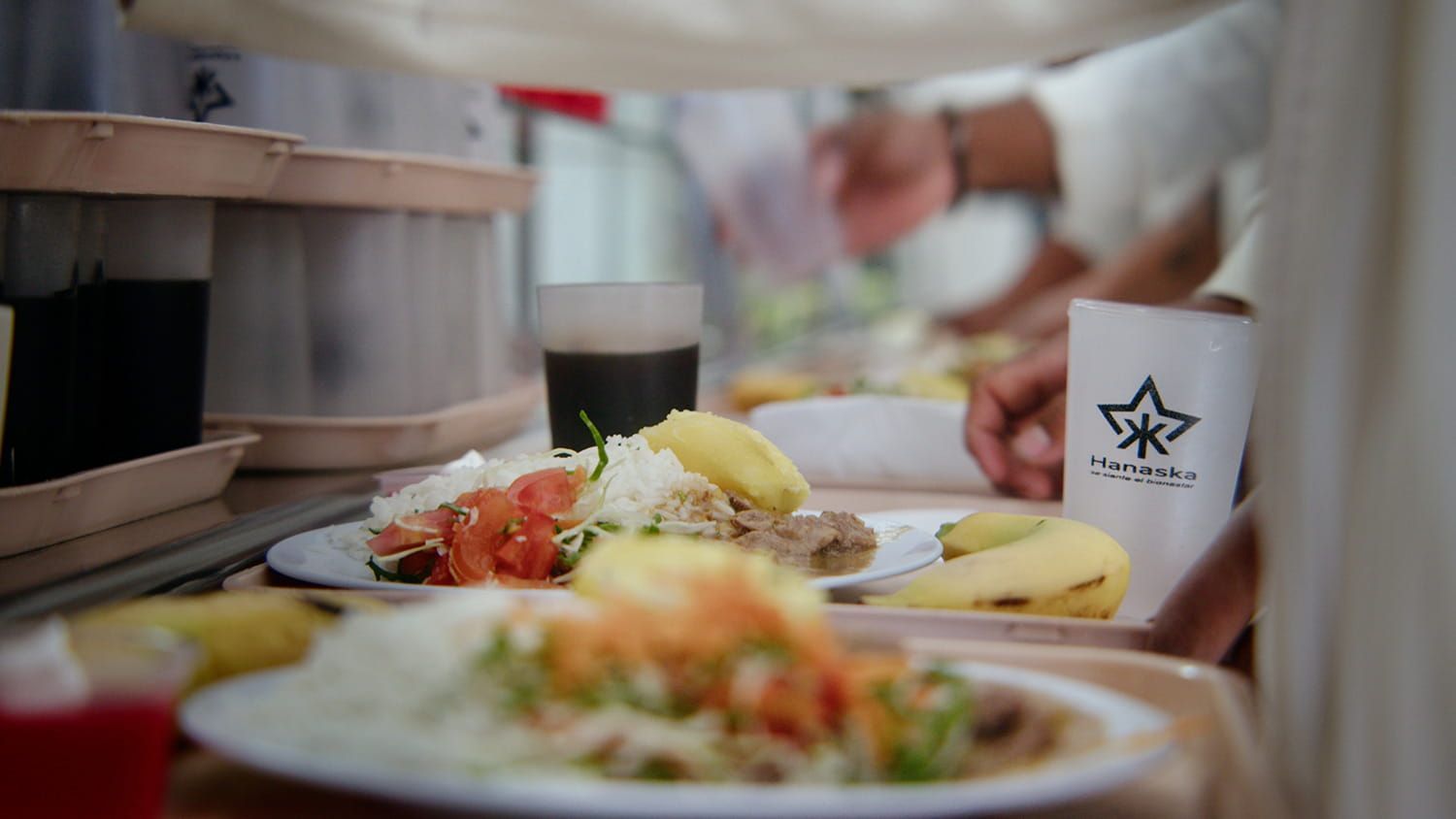 Platos de sushi en una cinta transportadora en un restaurante, con una mano que intenta alcanzar una taza que está al lado.