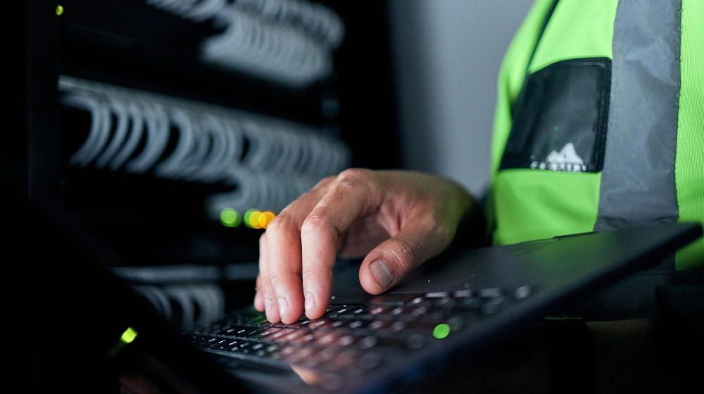 Mano con chaleco de seguridad verde neón usando un teclado en una sala de servidores con poca luz