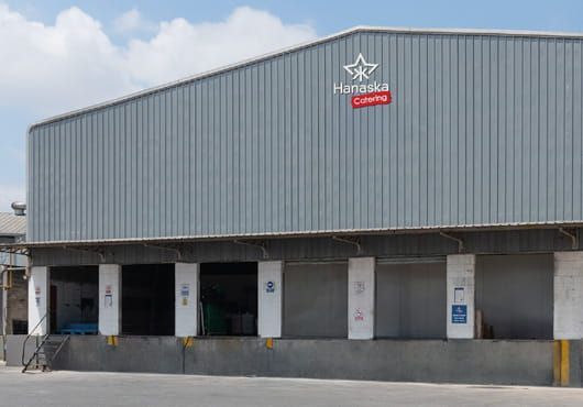 Muelle de carga de almacén industrial con revestimiento de metal gris y múltiples puertas de acceso bajo un gran voladizo de techo.