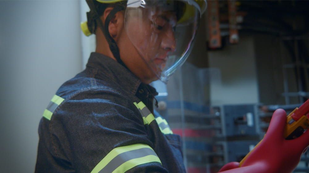 Trabajador con casco y protector facial manipulando equipos en un entorno industrial.