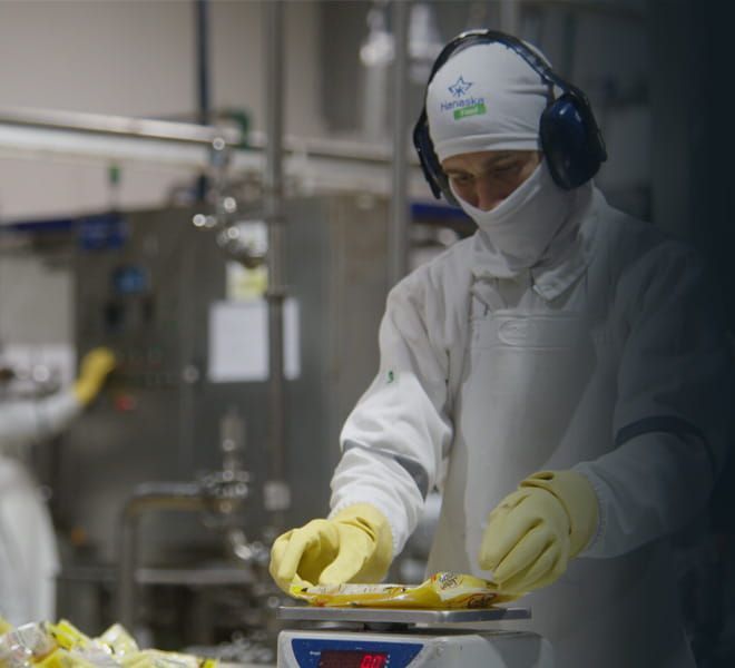 Trabajador con traje protector blanco y guantes amarillos manipulando alimentos en una instalación industrial limpia.