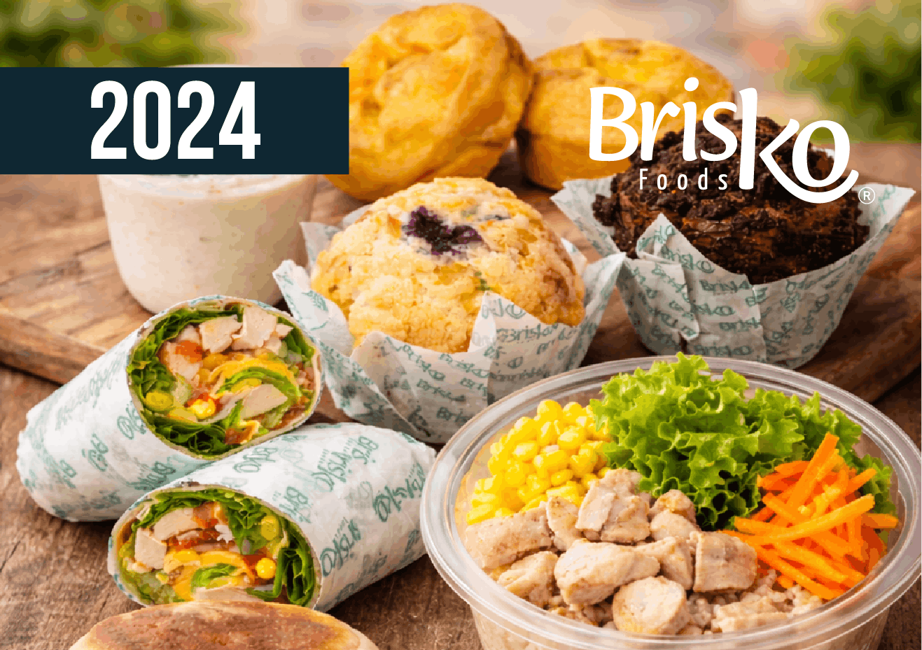Anuncio de Brisko Foods de 2024 con wraps, muffins y un tazón de ensalada sobre una mesa de madera.
