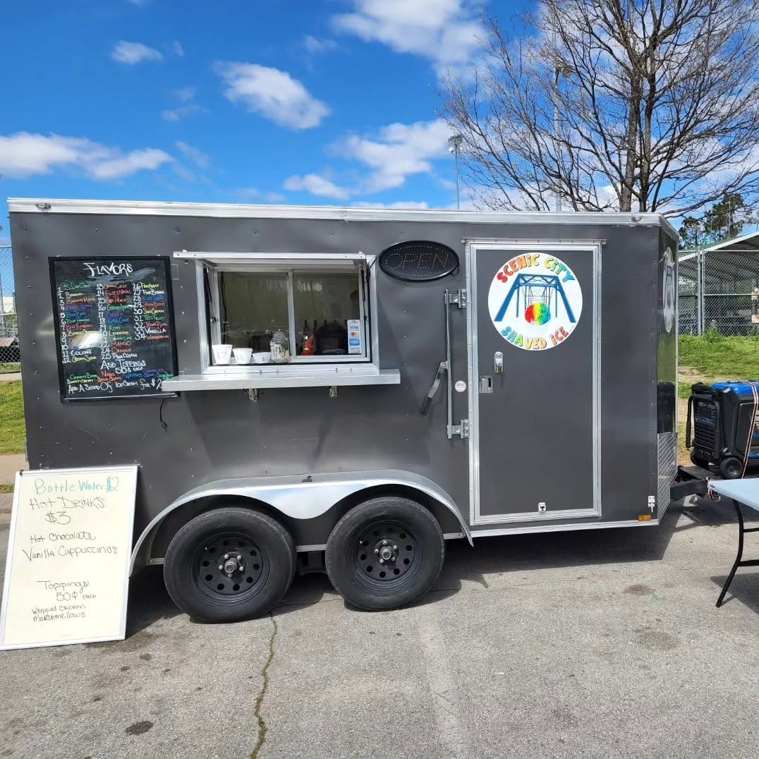 Gray food trailer with serving window and colorful logo, parked outdoors on a sunny day