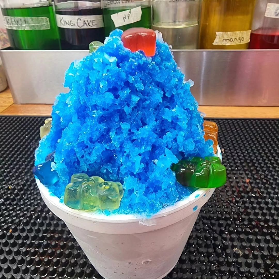 Blue shaved-ice dessert in a white cup, topped with gummy candies on a counter.