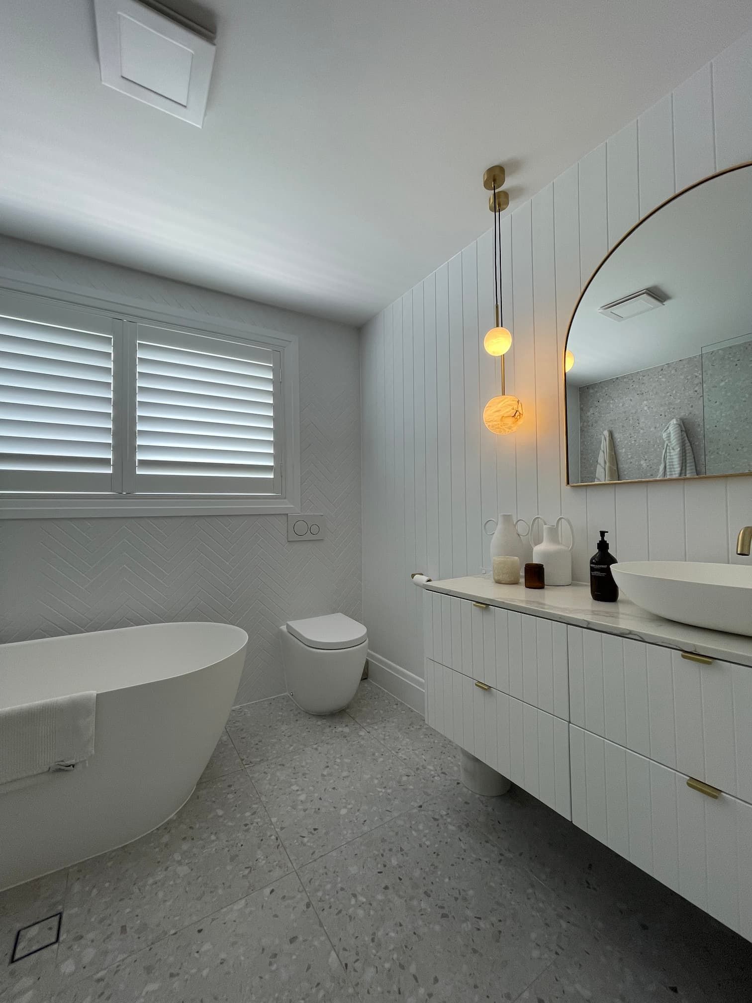 Modern white bathroom with freestanding tub, floating vanity, and large round mirror.