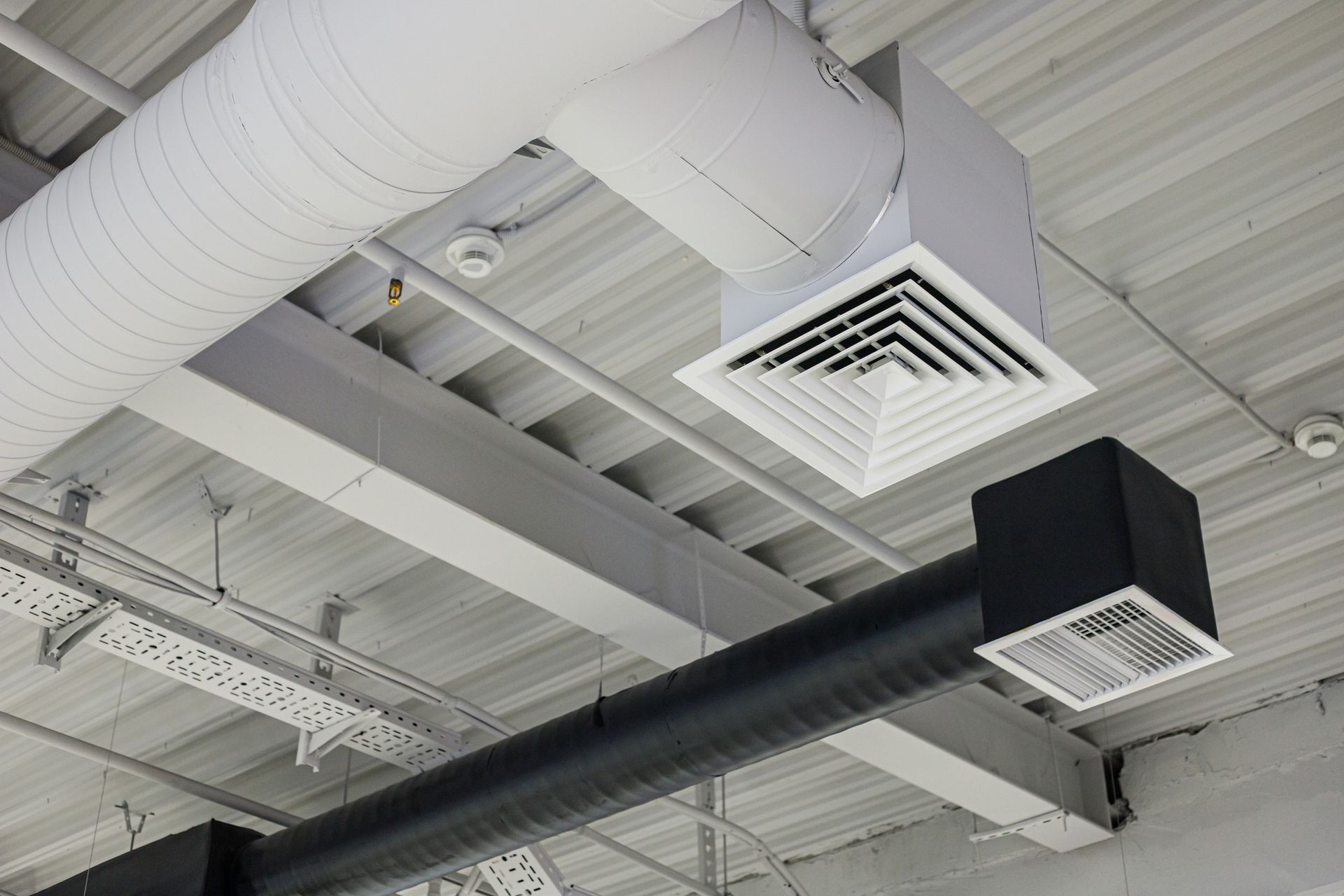 A commercial ceiling ductwork with a square air diffuser and round supply duct