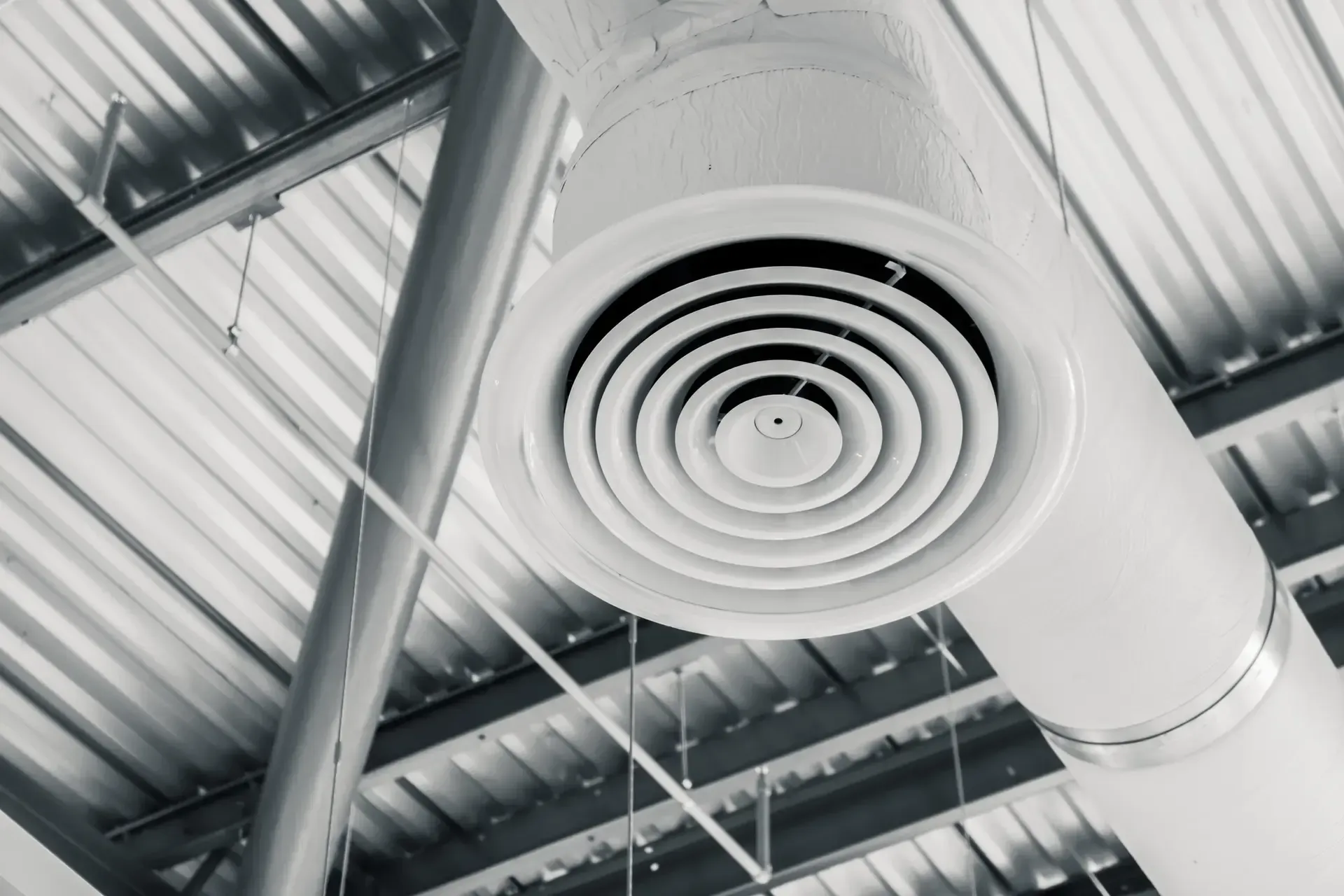 White air vent on a ceiling in a commercial building, with metal beams and ductwork visible.