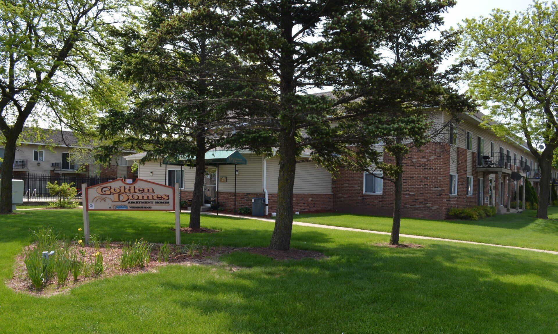 Golden Domes Apartments property with green grass, pathways, and trees.