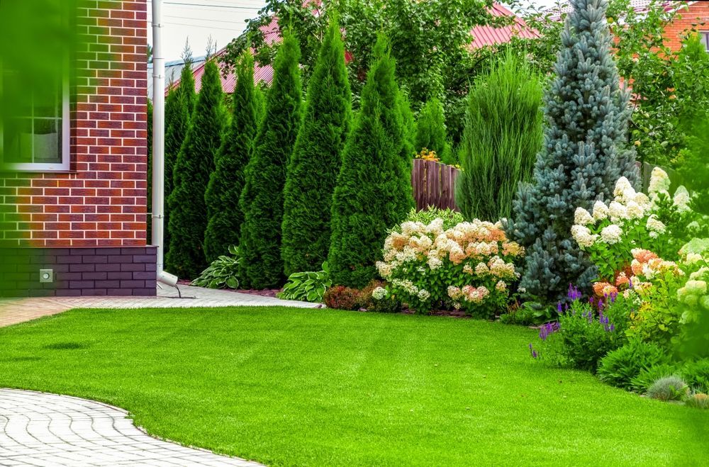 A lush green lawn with trees and flowers in front of a brick house.