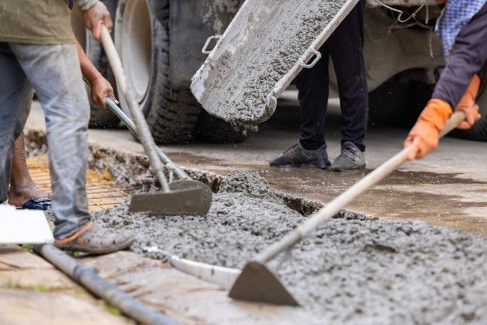 Workers leveling concrete from a truck using shovels on a construction site.