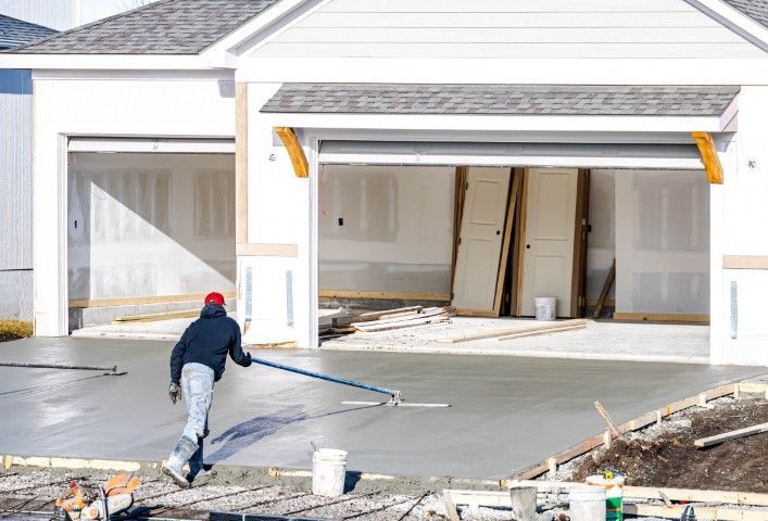 A construction worker smoothing wet concrete driveway in front of a house under construction.