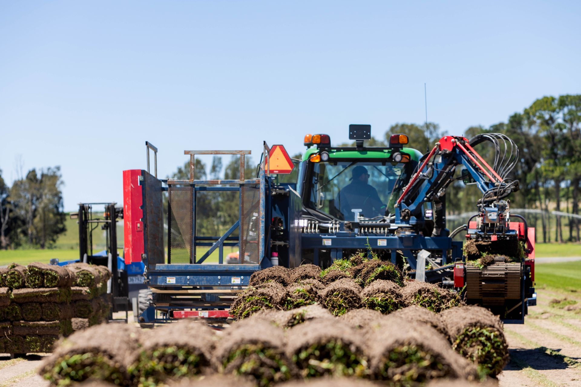 Tractor harvesting rolled sod on a field under a blue sky.