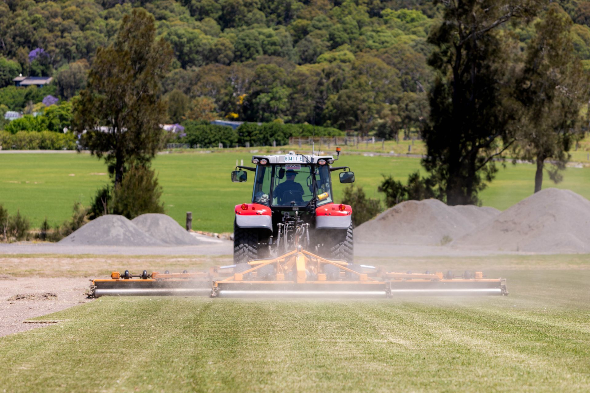 A tractor mowing a field, raising dust. Mountains and trees in the background.