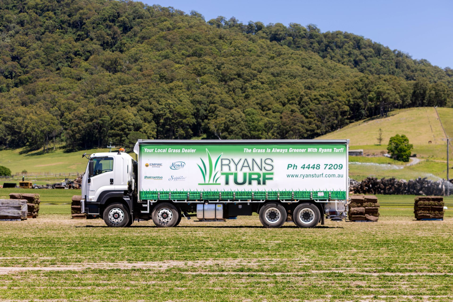 A white Ryans Turf truck in a field, green signage, green hills in background.