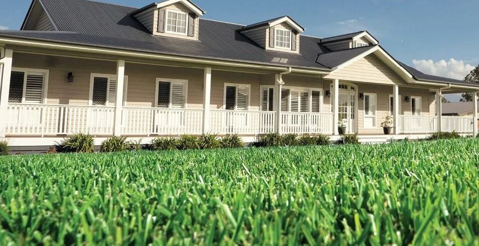 A tan house with a white porch and dark gray roof with green grass