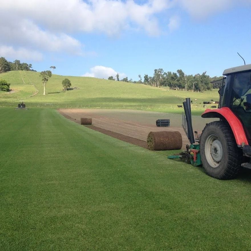 A tractor laying sod rolls on a green field under a blue sky.