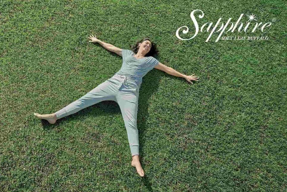 Woman lying on green grass with arms and legs outstretched;