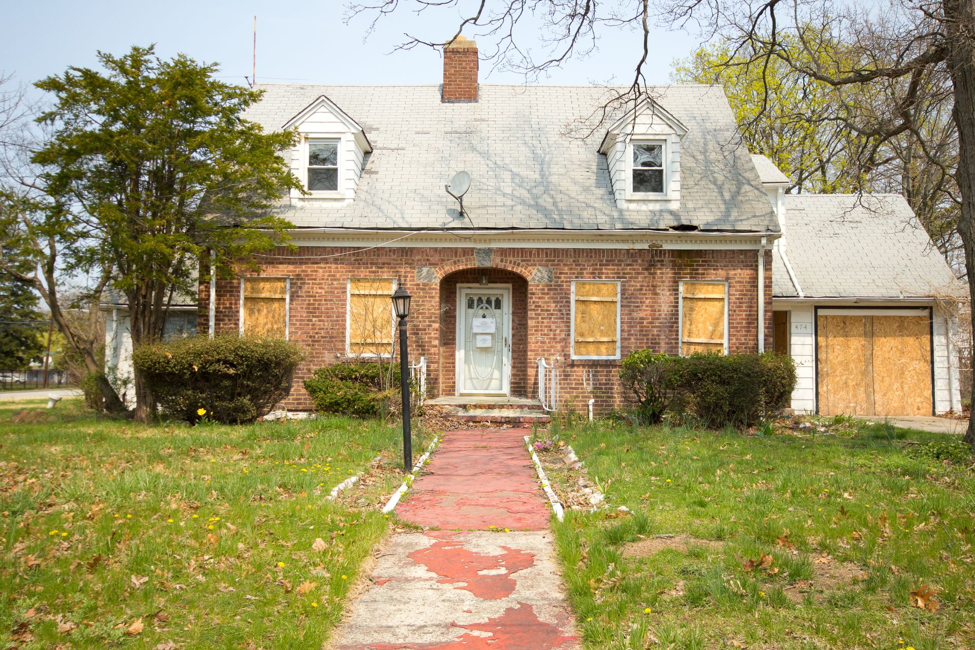 Brick house with a gray roof, front walkway, and detached garage surrounded by trees and lawn