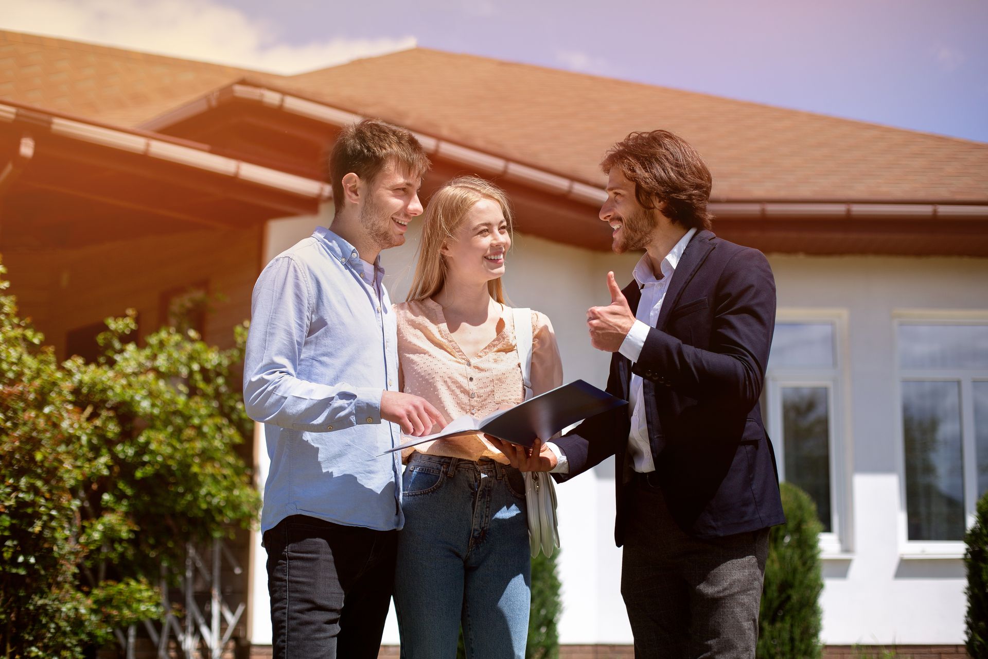 Three people reviewing documents outside a house, smiling and talking in sunlight.