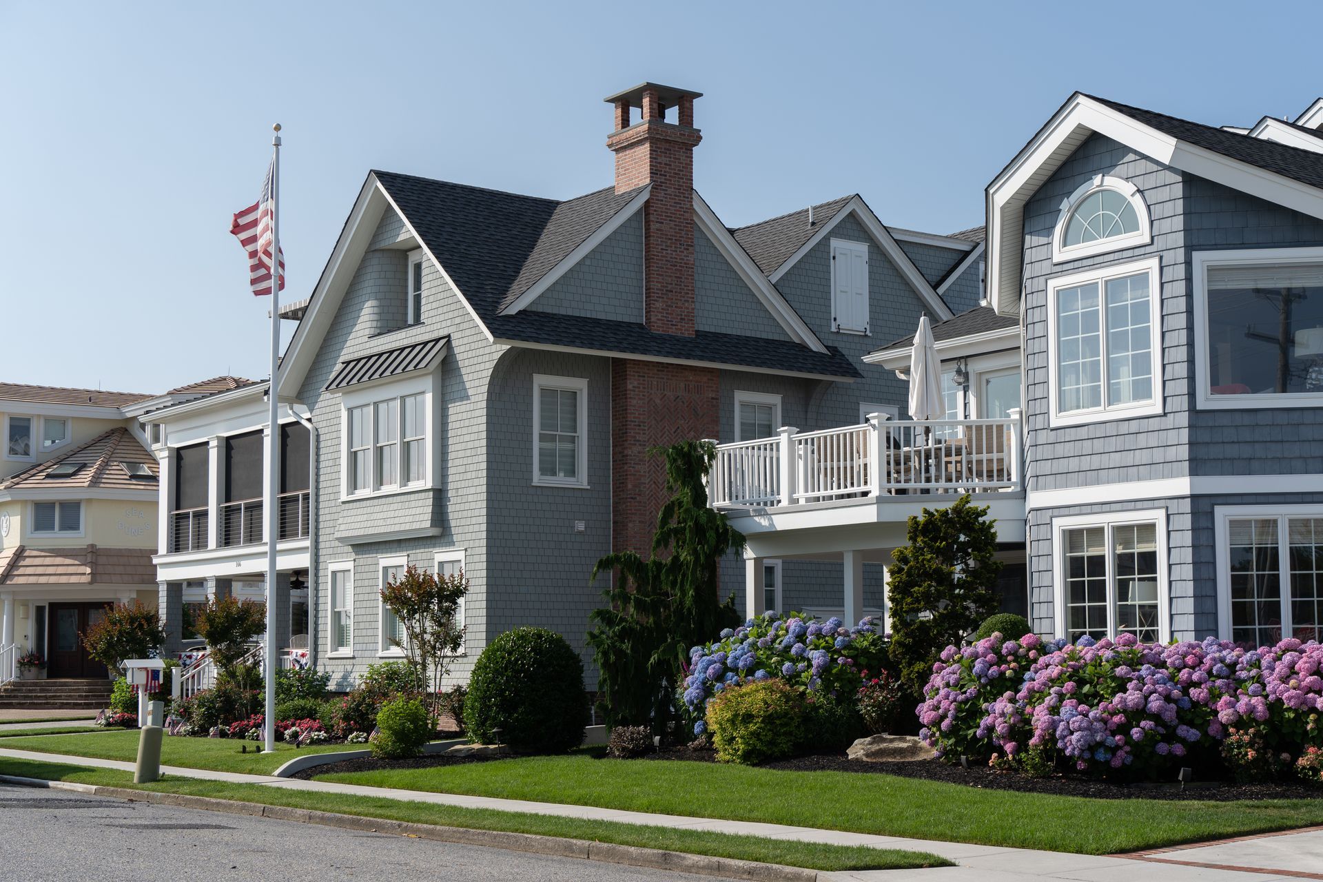 Row of coastal-style houses with balconies, flowers, and an American flag under a clear blue sky