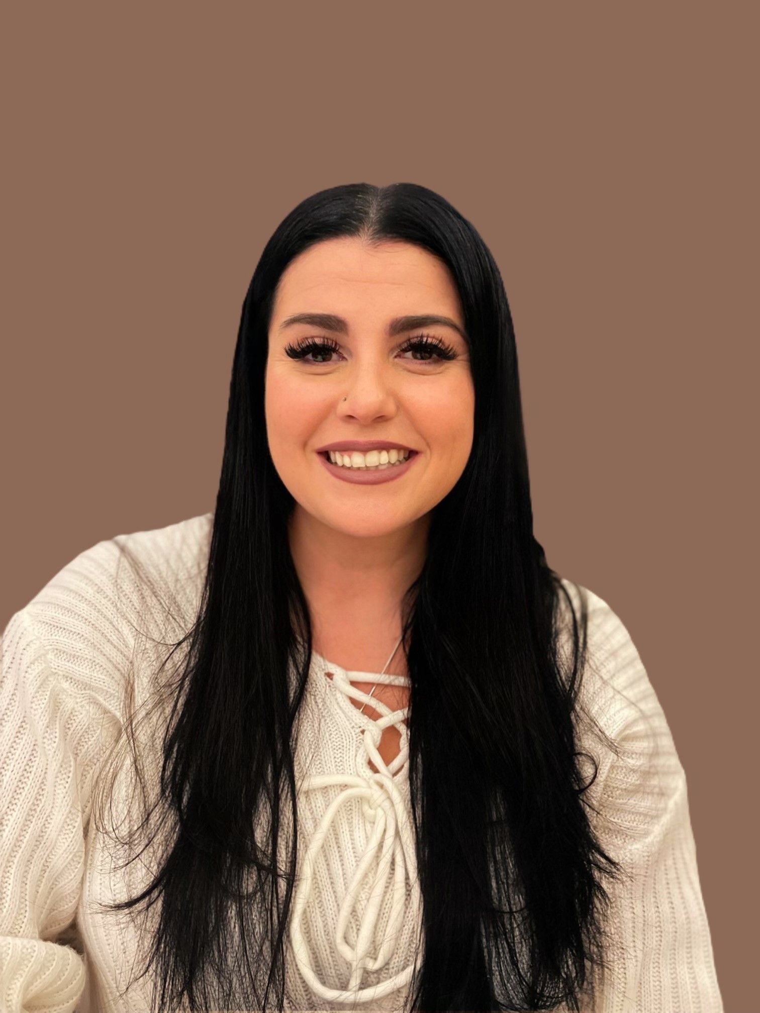 Woman with dark hair smiles, wearing a cream-colored sweater. Brown background.